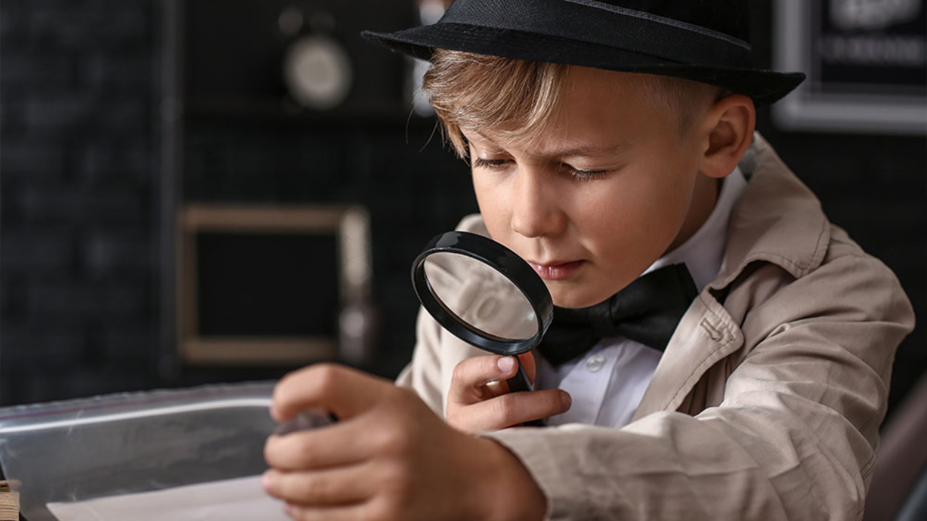 Niño pequeño disfrazado de detective con una lupa inspeccionando una evidencia