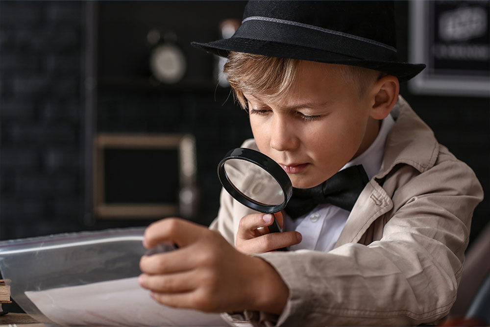 Niño pequeño disfrazado de detective con una lupa inspeccionando una evidencia